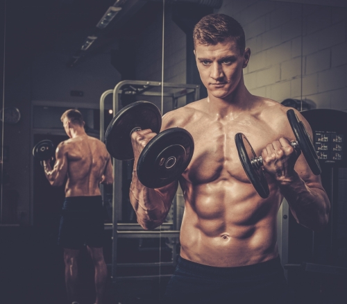 Athletic man doing exercises with dumbbells in The Gym's Studio